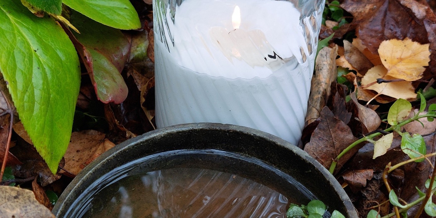 Kerze und Wasser am Grab mit Laub